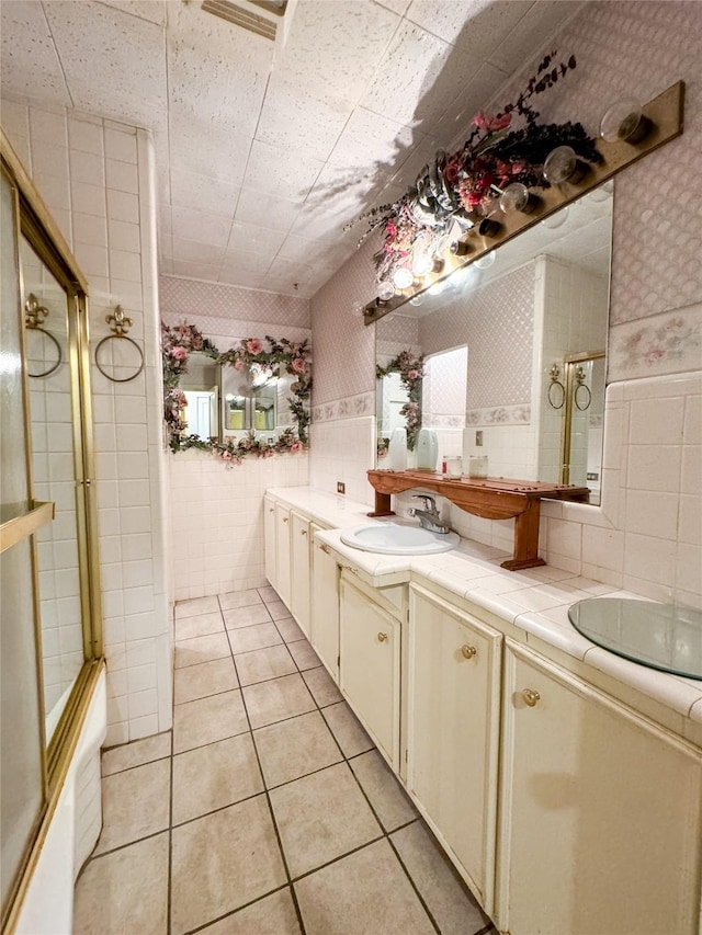 full bathroom with tile patterned flooring, a sink, tile walls, double vanity, and wallpapered walls