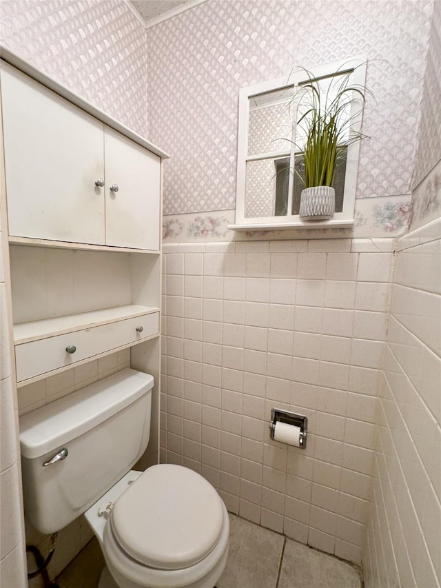 bathroom with a wainscoted wall, tile walls, wallpapered walls, toilet, and tile patterned floors