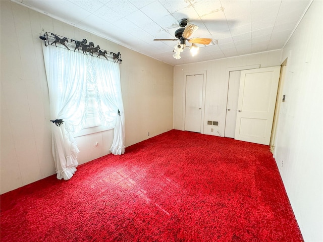 unfurnished bedroom with two closets, ceiling fan, visible vents, and carpet flooring