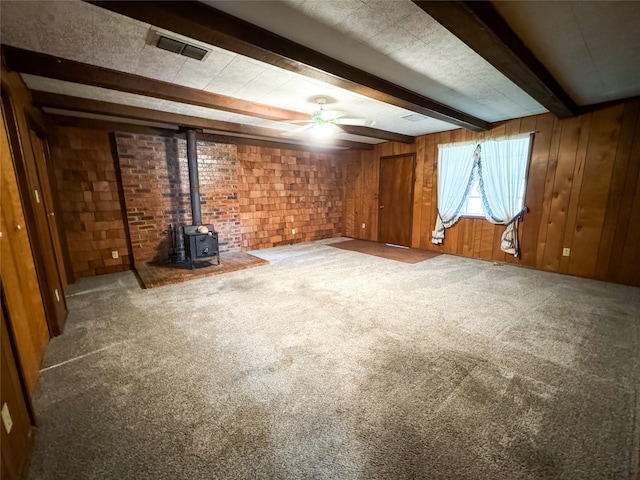 unfurnished living room with visible vents, beamed ceiling, a wood stove, carpet flooring, and wood walls