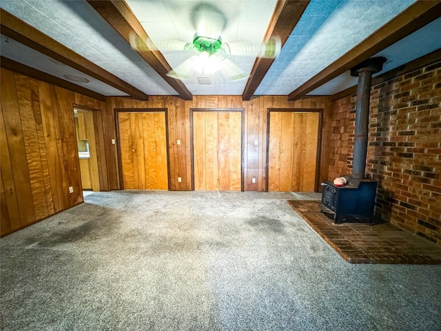 interior space featuring a wood stove, dark carpet, and wood walls