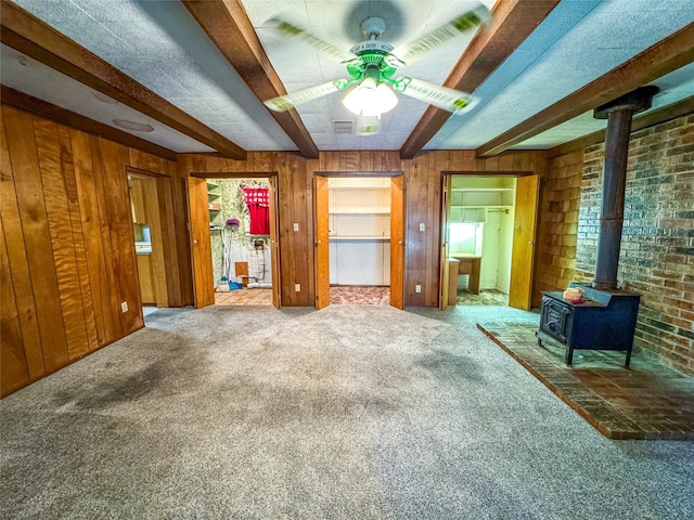 unfurnished room with a wood stove, wooden walls, carpet floors, and beam ceiling