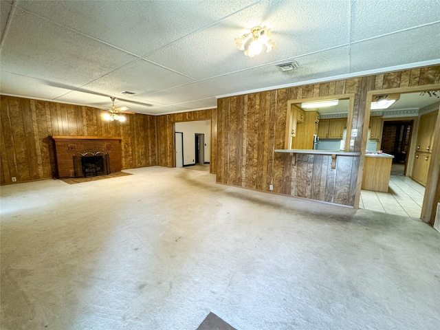 unfurnished living room featuring light carpet, wooden walls, visible vents, a ceiling fan, and a fireplace