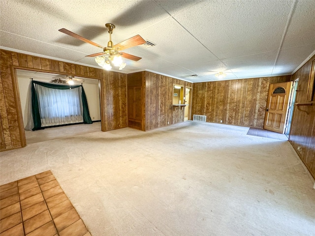 empty room with visible vents, light colored carpet, ceiling fan, and wooden walls