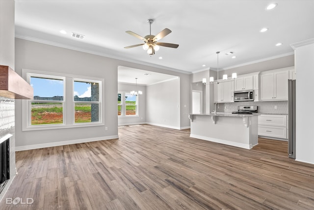 unfurnished living room featuring sink, ceiling fan with notable chandelier, hardwood / wood-style flooring, and crown molding