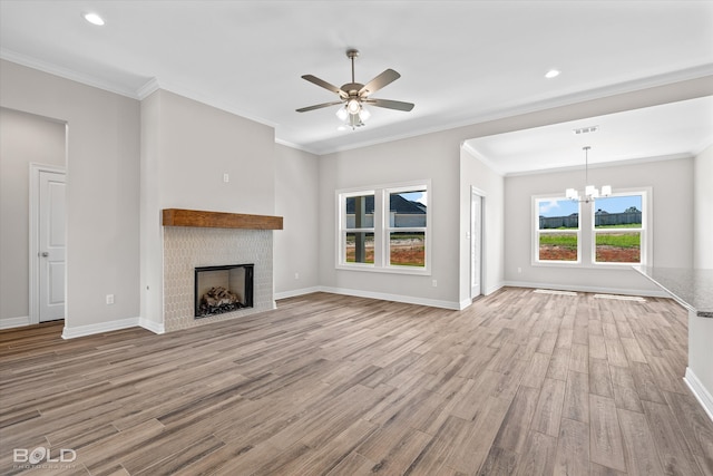 unfurnished living room with a tiled fireplace, ceiling fan with notable chandelier, ornamental molding, and light hardwood / wood-style floors