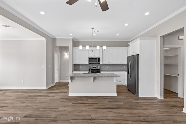 kitchen featuring decorative backsplash, ceiling fan, a kitchen island with sink, stainless steel appliances, and wood-type flooring