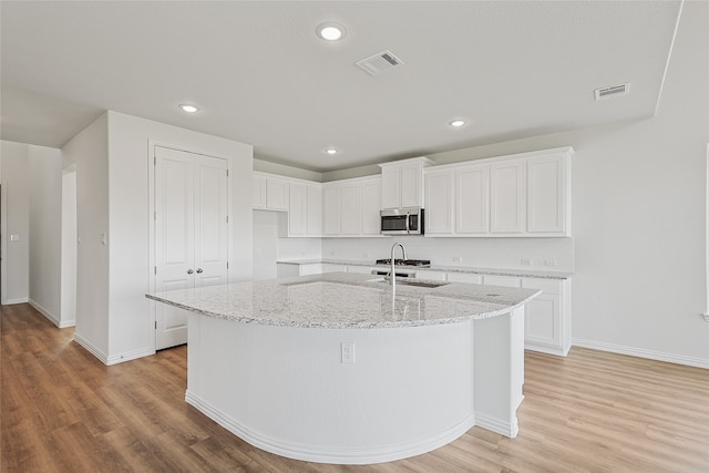 kitchen with a kitchen island with sink, sink, light stone countertops, light wood-type flooring, and white cabinetry