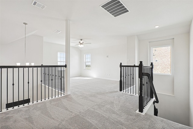 corridor featuring carpet floors, visible vents, vaulted ceiling, and an upstairs landing