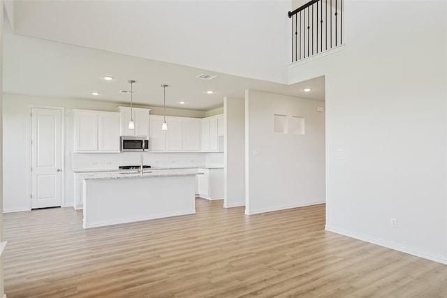 kitchen with a center island with sink, decorative light fixtures, white cabinets, light stone counters, and light hardwood / wood-style floors