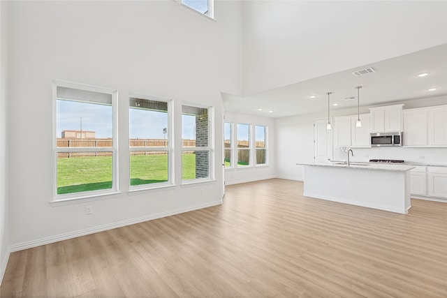 unfurnished living room with a towering ceiling, sink, and light wood-type flooring