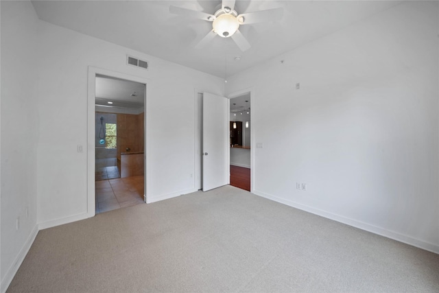 unfurnished bedroom featuring visible vents, baseboards, a ceiling fan, ensuite bath, and carpet