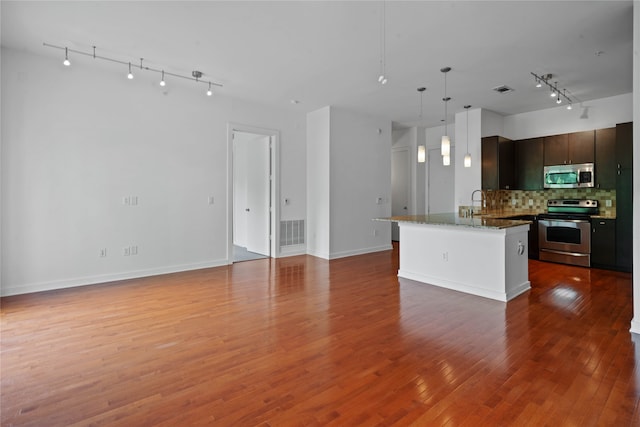 kitchen with tasteful backsplash, rail lighting, stainless steel appliances, hardwood / wood-style floors, and stone countertops