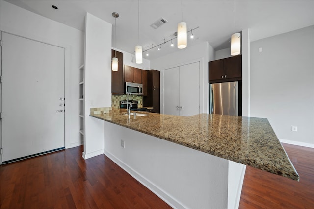 kitchen featuring appliances with stainless steel finishes, kitchen peninsula, backsplash, dark hardwood / wood-style floors, and dark stone countertops