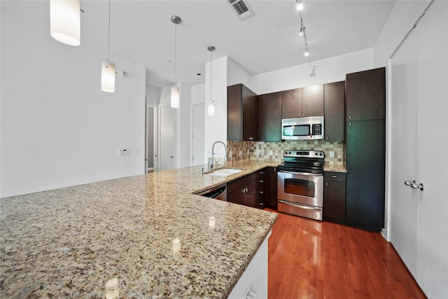 kitchen with dark wood-type flooring, stainless steel appliances, light stone countertops, decorative backsplash, and sink