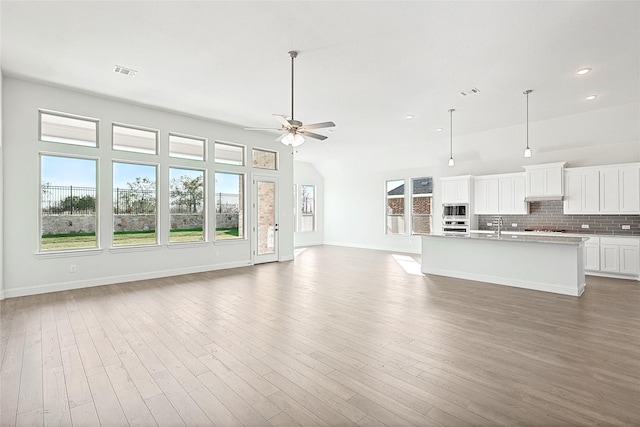 unfurnished living room featuring a healthy amount of sunlight, visible vents, and dark wood-style flooring