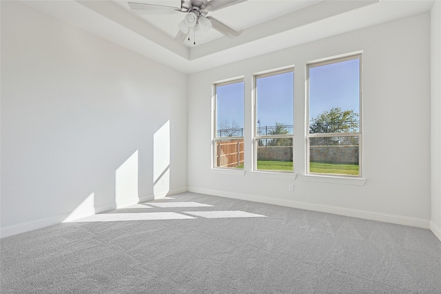 unfurnished room featuring ceiling fan, baseboards, a tray ceiling, and light colored carpet