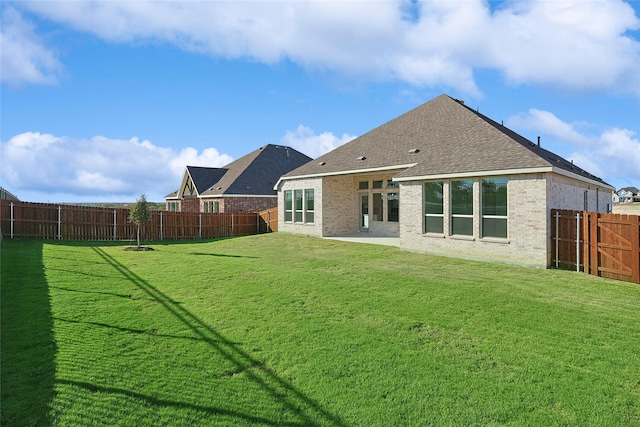 back of house with a fenced backyard, a lawn, and brick siding