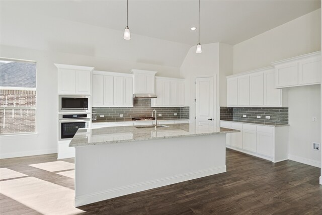 kitchen with hanging light fixtures, a kitchen island with sink, white cabinetry, stainless steel oven, and built in microwave