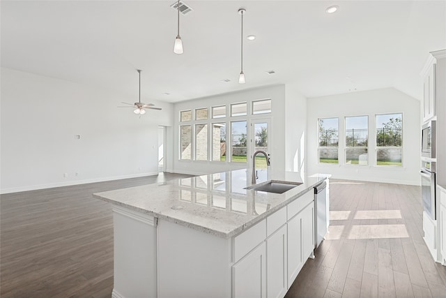 kitchen featuring light stone counters, a sink, open floor plan, appliances with stainless steel finishes, and an island with sink