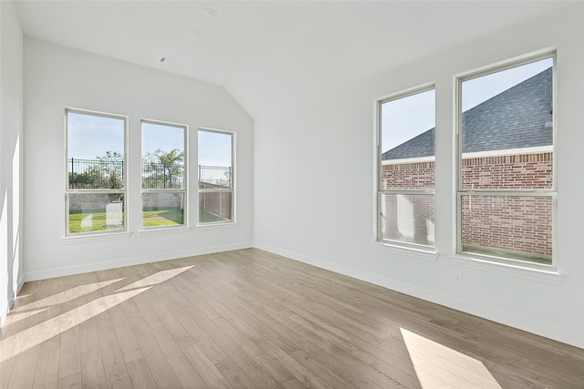 spare room featuring vaulted ceiling, light wood-style flooring, and baseboards