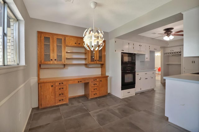 kitchen featuring white cabinetry, built in desk, pendant lighting, ceiling fan with notable chandelier, and black appliances