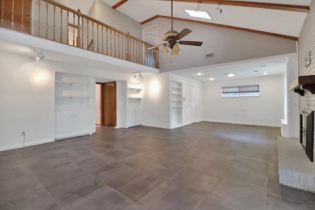 unfurnished living room with built in features, a fireplace, a skylight, beamed ceiling, and ceiling fan