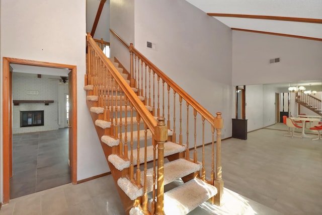 stairway with ceiling fan with notable chandelier, a fireplace, and high vaulted ceiling