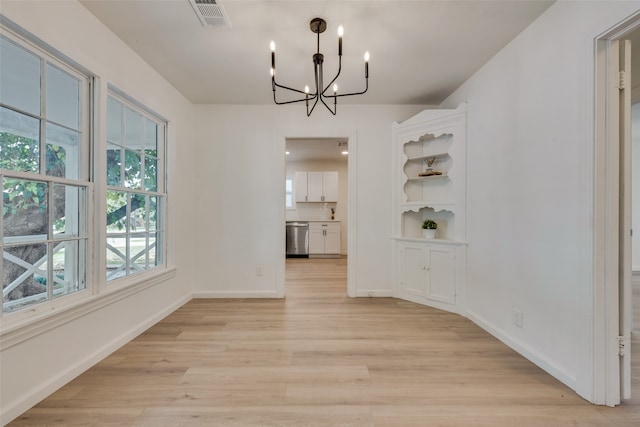 unfurnished dining area with an inviting chandelier and light hardwood / wood-style flooring