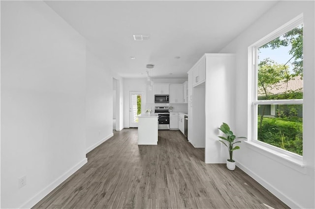 kitchen with white cabinets, a kitchen island, stainless steel appliances, wood-type flooring, and decorative light fixtures