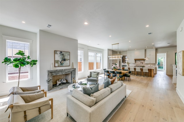 living room featuring a high end fireplace, a chandelier, light wood-type flooring, and a healthy amount of sunlight