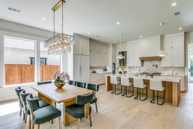 dining room with a notable chandelier, sink, and light wood-type flooring