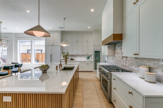 kitchen with tasteful backsplash, sink, light wood-type flooring, high end stainless steel range, and custom range hood