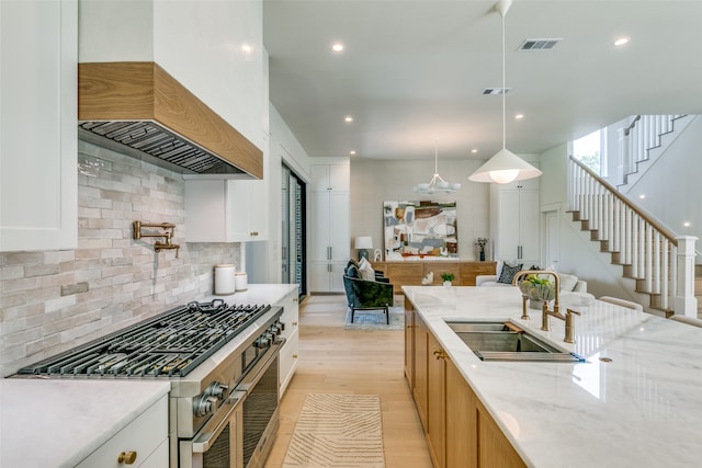 kitchen with light wood-type flooring, white cabinets, light stone counters, decorative backsplash, and double oven range