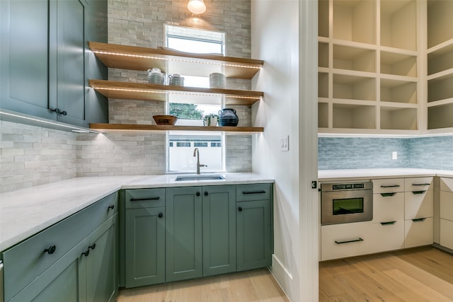 kitchen with light hardwood / wood-style flooring, tasteful backsplash, green cabinets, oven, and sink