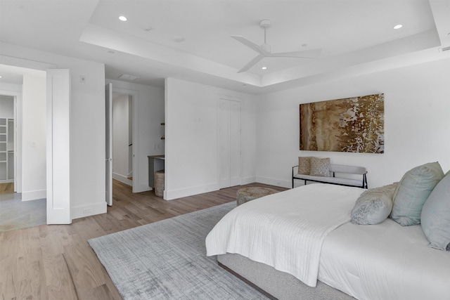 bedroom with ceiling fan, a raised ceiling, light hardwood / wood-style flooring, and a closet