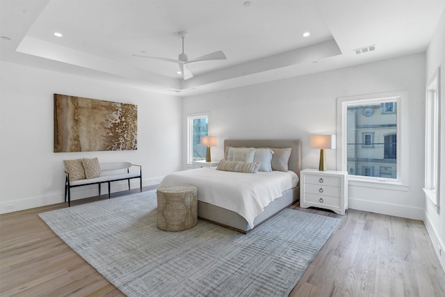 bedroom featuring ceiling fan, light hardwood / wood-style flooring, and a tray ceiling