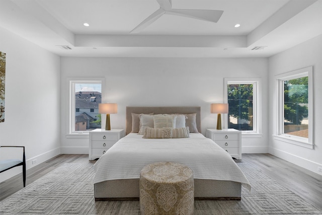 bedroom with ceiling fan, light wood-type flooring, and a raised ceiling