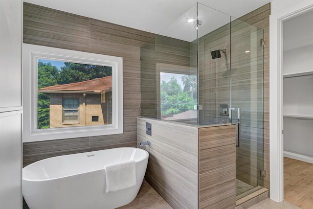 bathroom featuring plus walk in shower, plenty of natural light, and tile walls