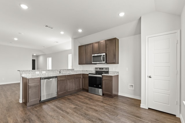 kitchen featuring kitchen peninsula, stainless steel appliances, dark brown cabinetry, light stone counters, and dark hardwood / wood-style flooring