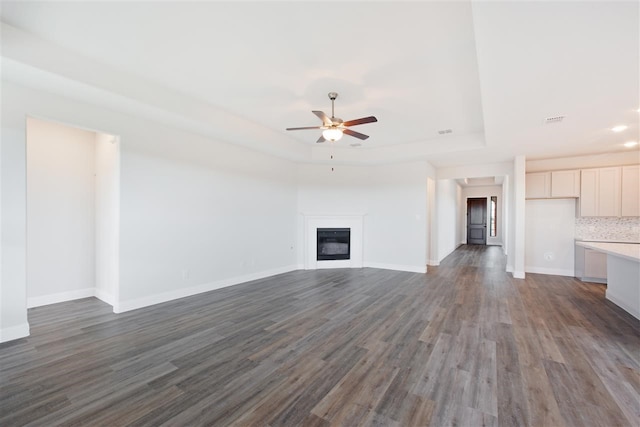 unfurnished living room featuring a tray ceiling, dark wood-type flooring, and ceiling fan