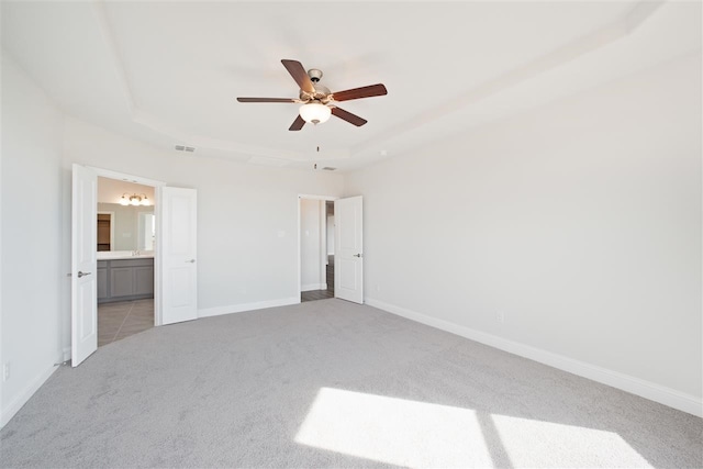 unfurnished bedroom with light tile patterned flooring, a tray ceiling, ensuite bathroom, and ceiling fan