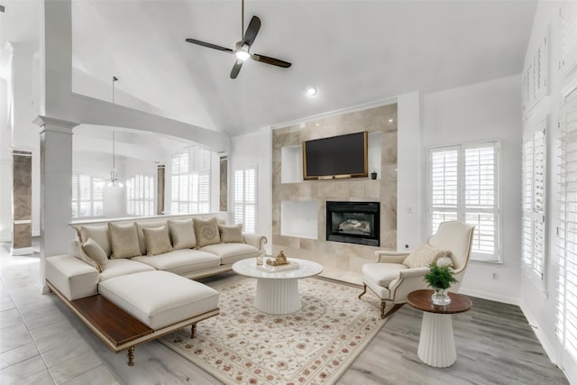 living room featuring light hardwood / wood-style flooring, decorative columns, lofted ceiling, a tiled fireplace, and ceiling fan with notable chandelier