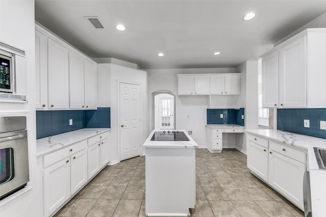 kitchen featuring white cabinets, oven, black electric stovetop, a kitchen island, and light stone counters