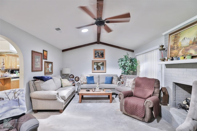 carpeted living room with lofted ceiling with beams, ceiling fan, and a brick fireplace