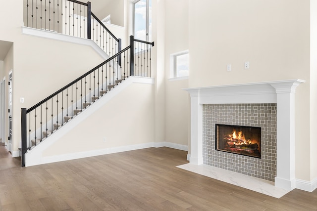 stairway with wood-type flooring, a tile fireplace, and a high ceiling