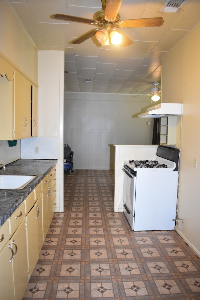 kitchen with a drop ceiling, ceiling fan, white range with gas stovetop, dark tile patterned flooring, and sink