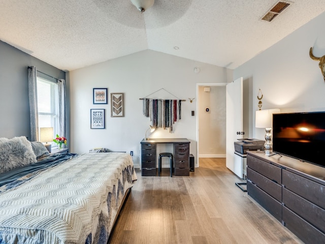 bedroom with ceiling fan, light hardwood / wood-style floors, vaulted ceiling, and a textured ceiling