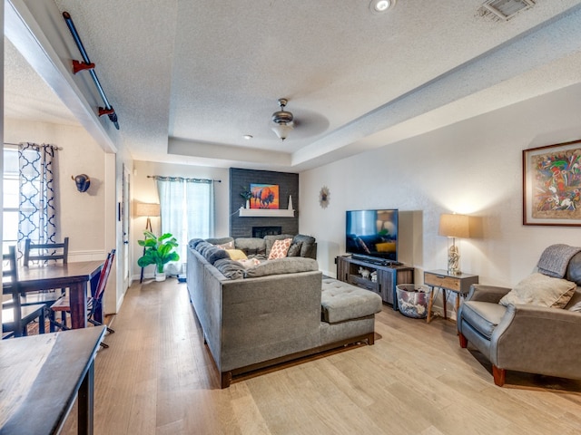 living room featuring a fireplace, light hardwood / wood-style flooring, ceiling fan, and a tray ceiling