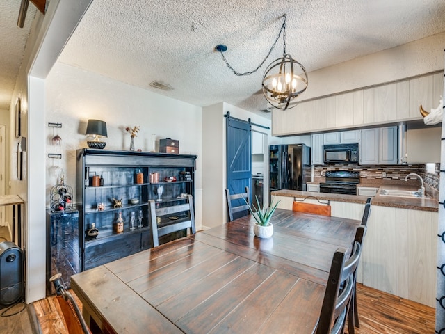 dining room with sink, a textured ceiling, wood-type flooring, and a barn door